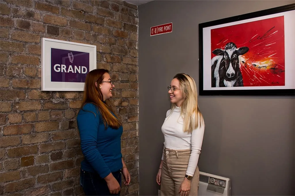Two students chatting in a hallway at ISI Dublin with exposed brick walls and Irish artwork.